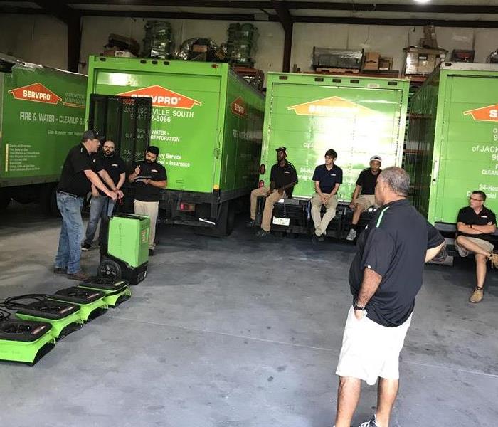 SERVPRO employees sitting around a garage on vehicles looking at equipment. 
