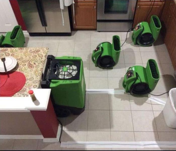 Air movers and dehumidifiers sitting in the floor of this kitchen